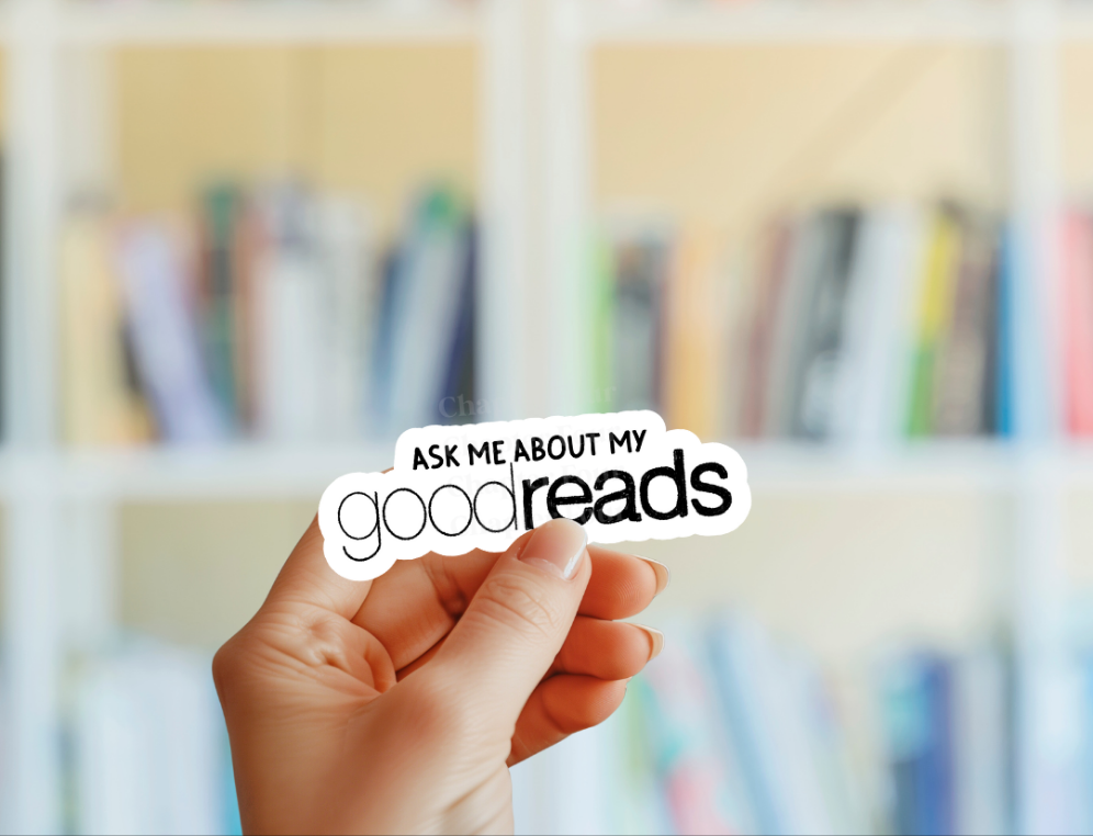 Hand holding a sticker with 'Ask me about my Goodreads' text in front of a blurred bookshelf.