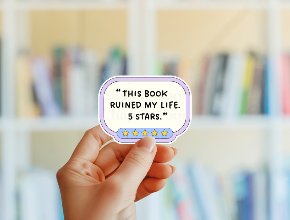 Hand holding a sticker with a humorous book review in front of a blurred bookshelf.