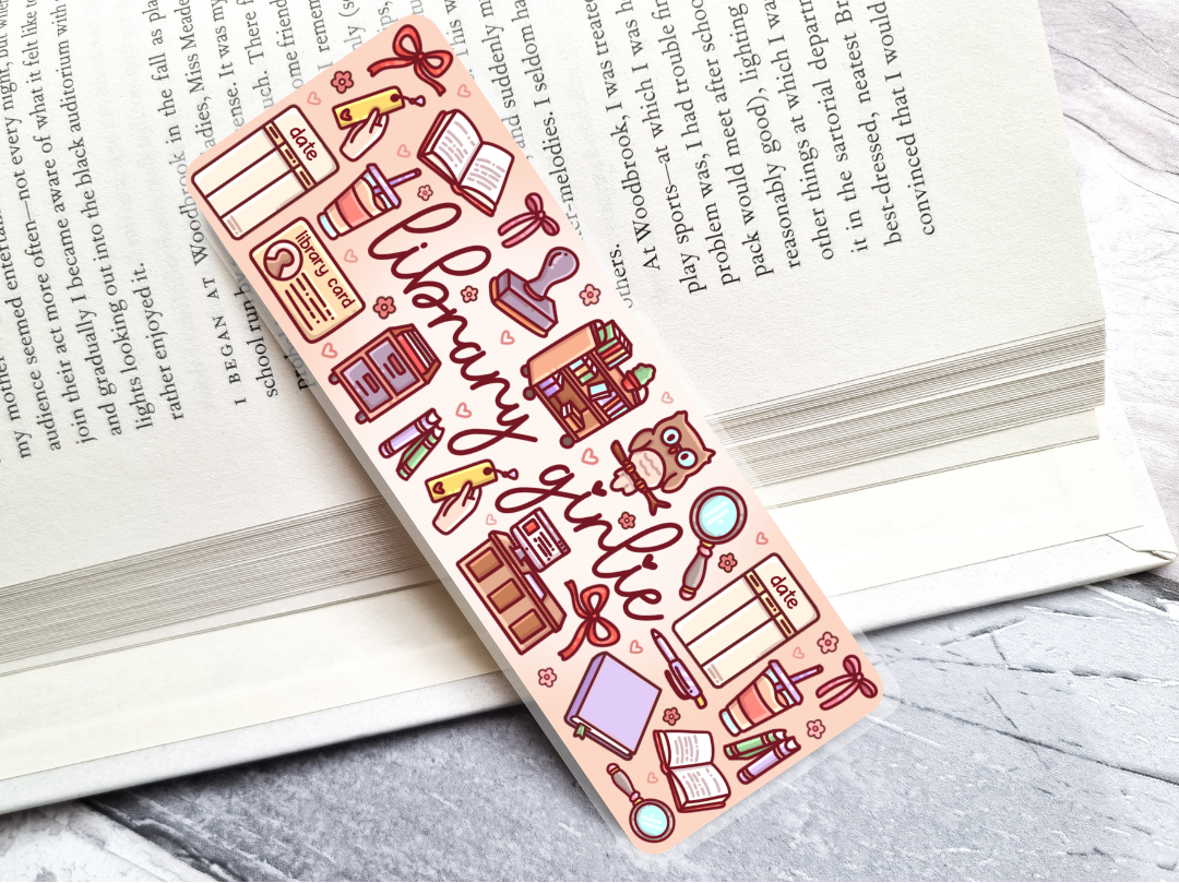 Colorful bookmark with library-themed illustrations and 'library girlie' text, laying on an open book