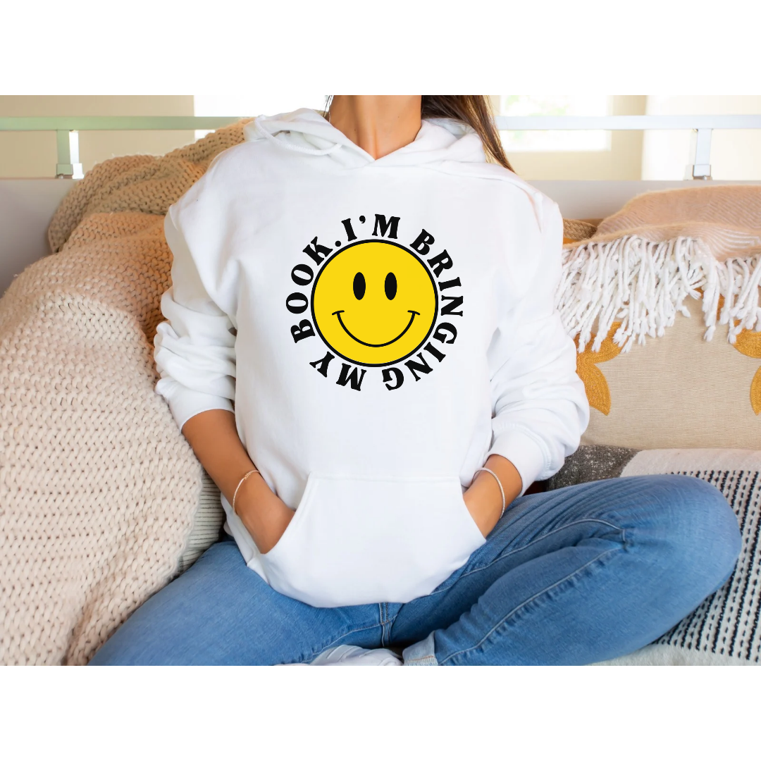 White Gildan 18500 Hoodie. Large yellow face with a smile. Font around the face is black and says I'm Bringing My Book.