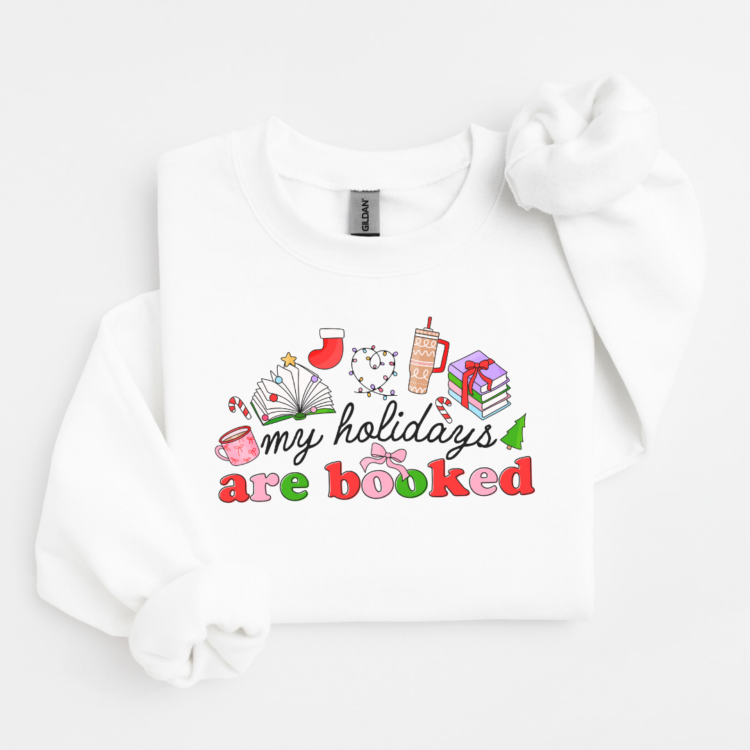 White 18000 gildan crewneck. Graphic says My Holidays Are Booked with tiny pictures of a pink mug, open book, Christmas stocking, Christmas lights, tumbler, and stack of books.