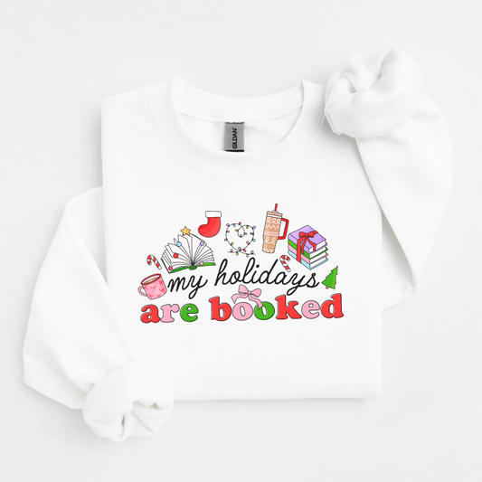 White 18000 gildan crewneck. Graphic says My Holidays Are Booked with tiny pictures of a pink mug, open book, Christmas stocking, Christmas lights, tumbler, and stack of books.