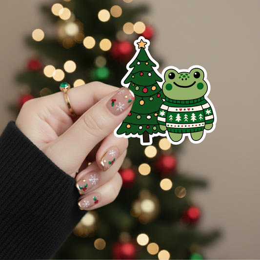 Hand holding a sticker of a frog and Christmas tree with a blurred Christmas tree in the background