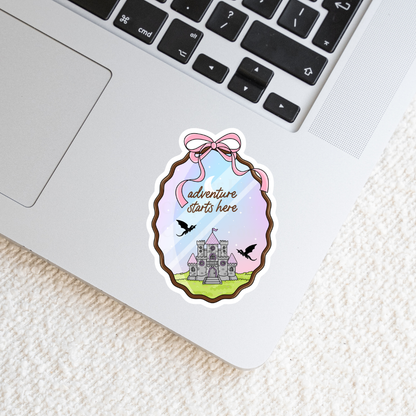 Sticker with castle design and 'adventure starts here' text on a laptop