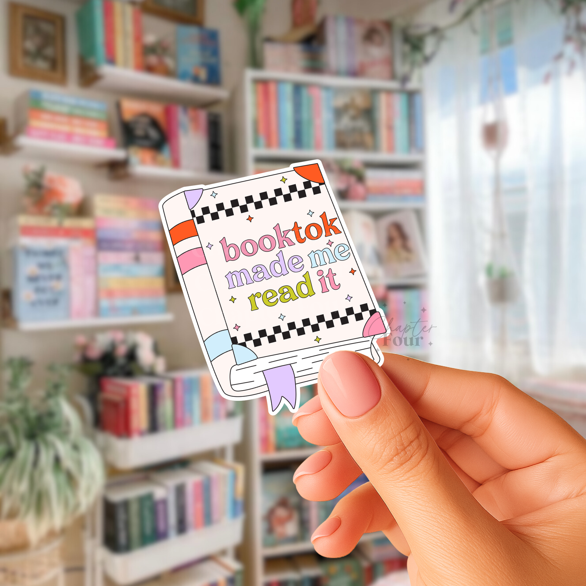 Hand holding a book-shaped sticker with 'booktok made me read it' text in a bookstore setting