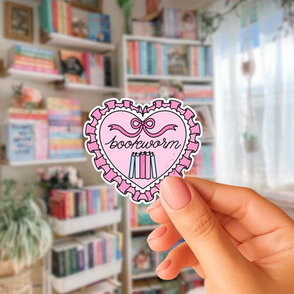 Pink and White Heart-shaped sticker with 'bookworm' cursive text held in front of a bookshelf.