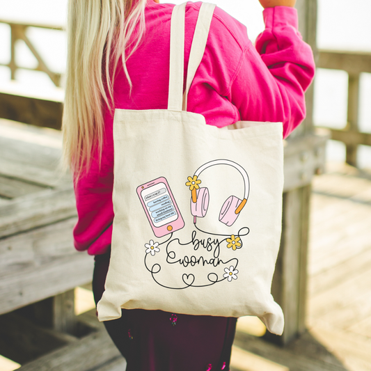 Person holding a tote bag with a 'busy woman' design near a wooden deck.
