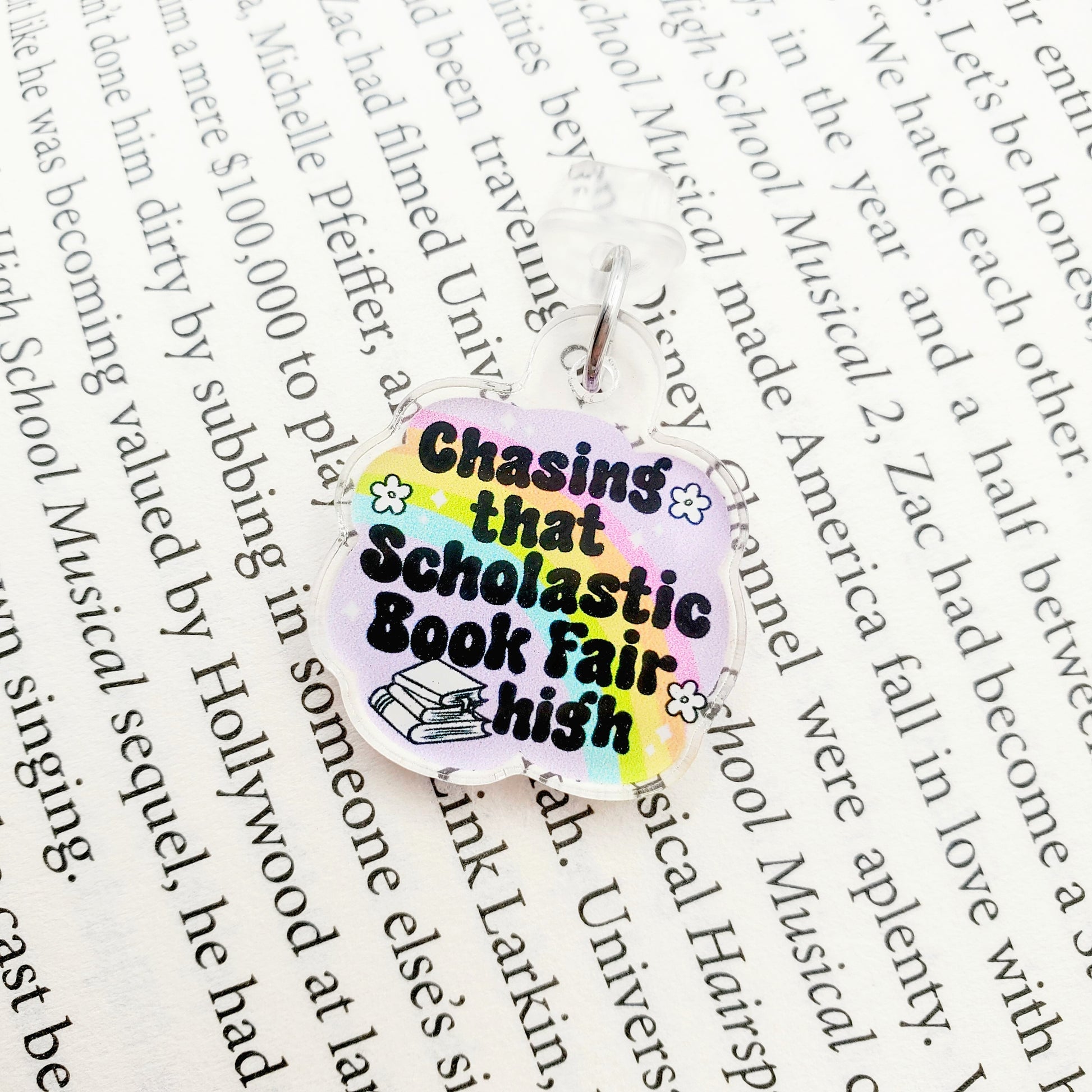 Colorful dust plug charm with text 'Chasing that Scholastic Book Fair high', laying on a paper background