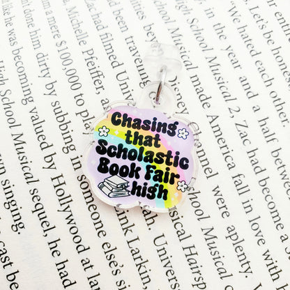 Colorful dust plug charm with text 'Chasing that Scholastic Book Fair high', laying on a paper background