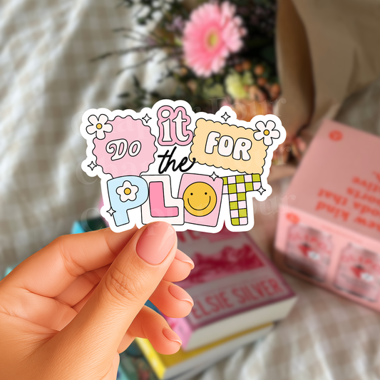 Hand holding a colorful sticker with 'do it for the plot' text and a smiley face, with books and flowers in the background.