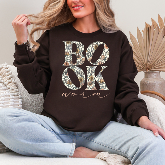 Person wearing a brown sweatshirt with floral 'BOOK worm' text, sitting on a couch.