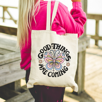 Person holding a tote bag with 'Good Things Are Coming' and butterfly design.