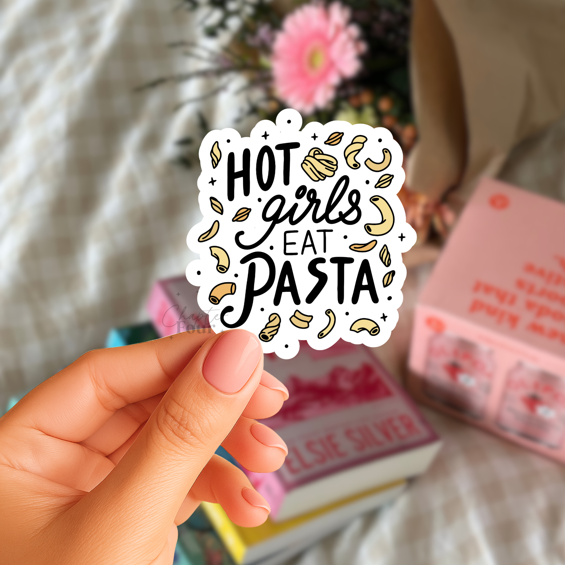 Hand holding a sticker with 'Hot girls eat pasta' text with noodle clip art surrounding it, against a blurred background