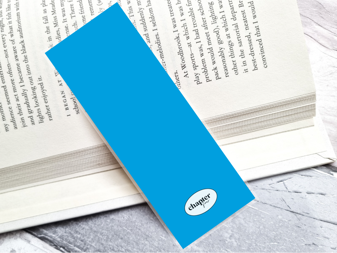 A bright blue bookmark back with a white oval 'chapter fourr' logo, resting diagonally on an open book on a gray marble surface.