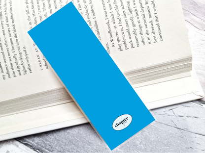 A bright blue bookmark back with a white oval 'chapter fourr' logo, resting diagonally on an open book on a gray marble surface.