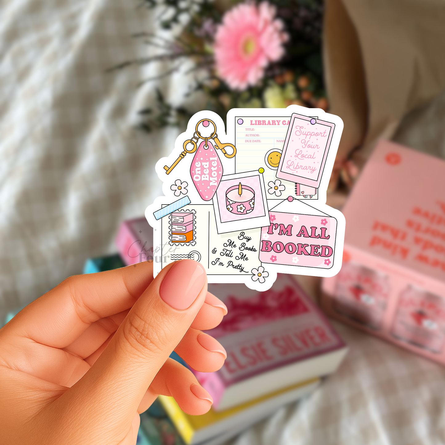 Hand holding a colorful sticker with 'I'm all booked' text and graphics, with books and flowers in the background.