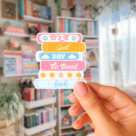 Colorful bookstack sticker with 'It's A Good Day To Read A Book' text held in front of a bookshelf.