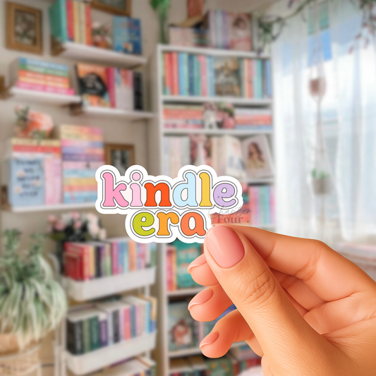 Hand holding a colorful 'kindle era' sticker in front of bookshelves