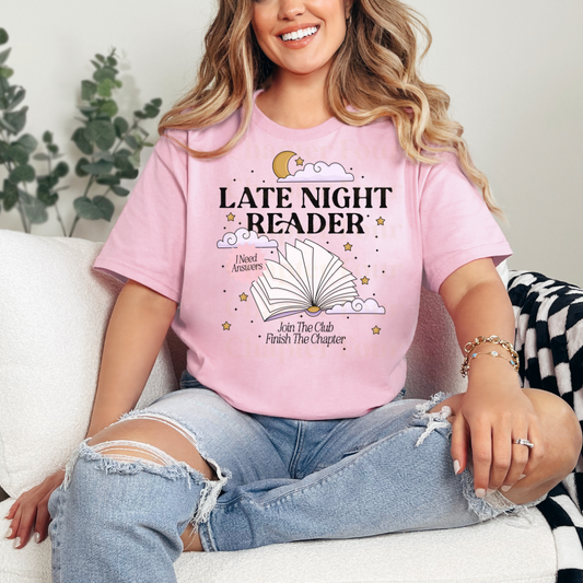 Person wearing a pink 'Late Night Reader' t-shirt sitting on a couch.