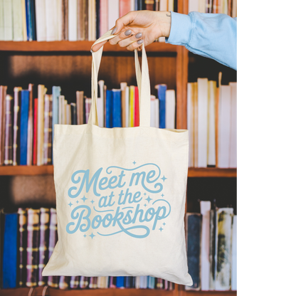 Tote bag with 'Meet me at the Bookshop' text held in front of a bookshelf.