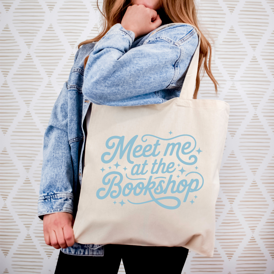 Person holding a tote bag with 'Meet me at the Bookshop' text against a textured white background