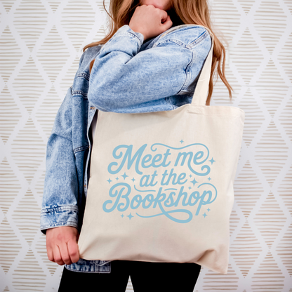 Person holding a tote bag with 'Meet me at the Bookshop' text against a textured white background