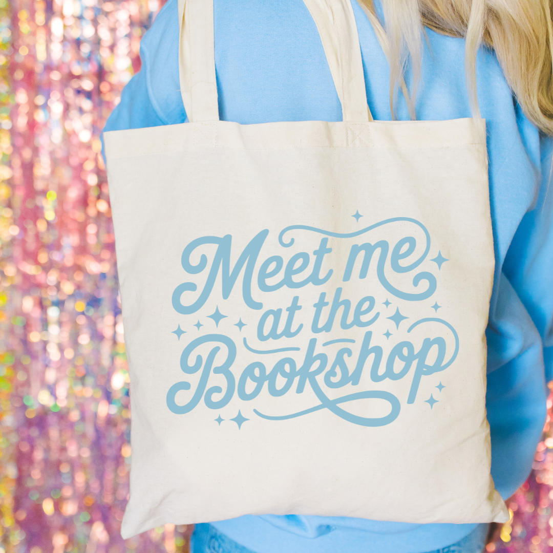 Tote bag with 'Meet me at the Bookshop' text held by a person against a colorful, blurred background.