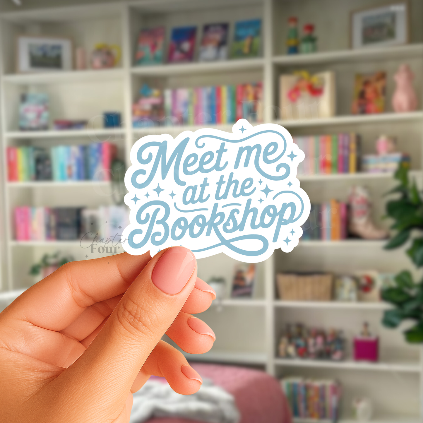 Hand holding a 'Meet me at the Bookshop' sticker with blue text,  in front of a bookshelf.