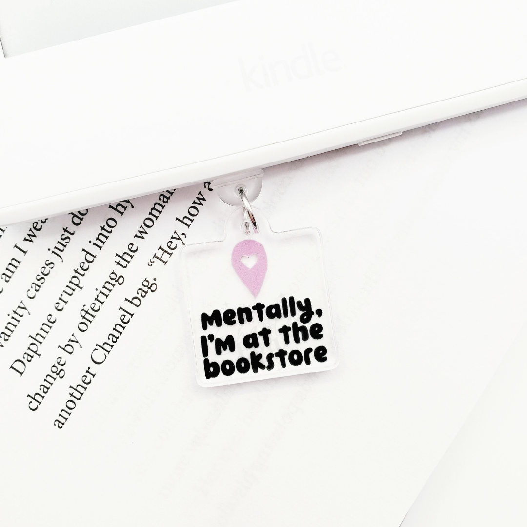 Dust plug charm with 'Mentally, I'm at the bookstore' text, laying on a book page