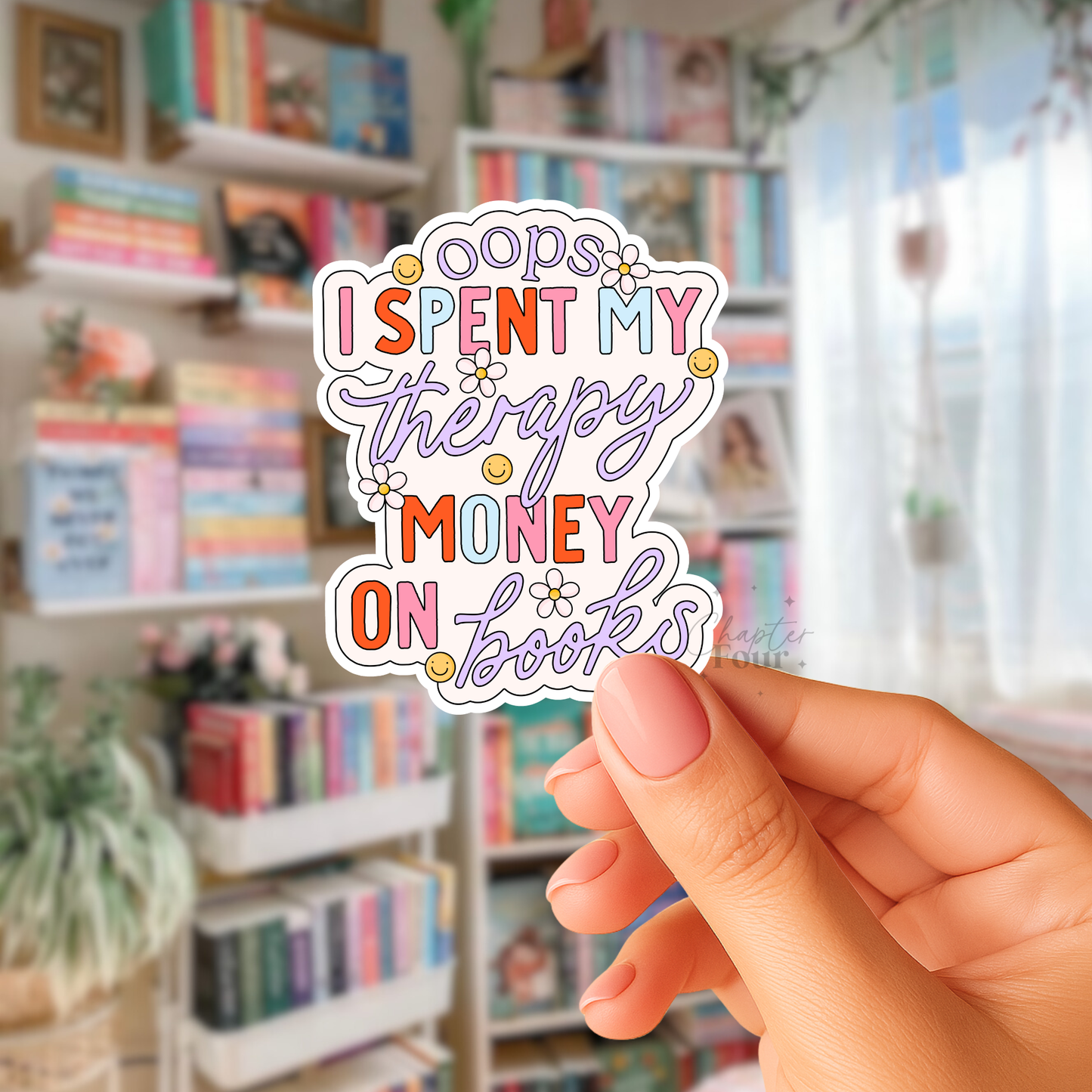 Hand holding a colorful sticker with 'Oops I spent my therapy money on books'  text in front of bookshelves