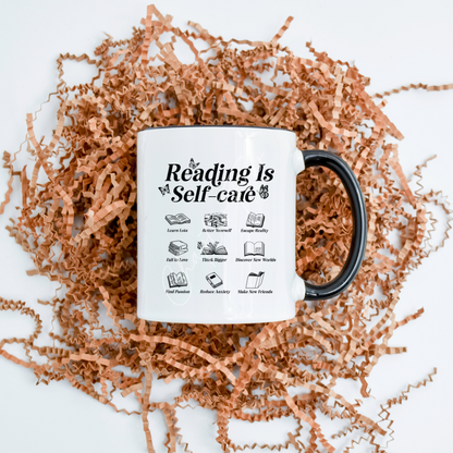 A white ceramic mug with black text and icons that say 'Reading Is Self-care' is displayed on a bed of brown shredded filling, emphasizing the mug's design and capacity of 11.8oz.