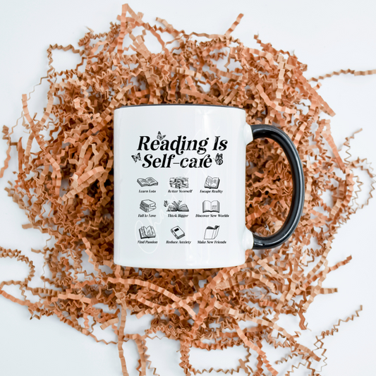 A white ceramic mug with black text and icons that say 'Reading Is Self-care' is displayed on a bed of brown shredded filling, emphasizing the mug's design and capacity of 11.8oz.