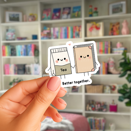 Hand holding a sticker with cartoon tea bag and book character with text below that says 'Better together' in front of a bookshelf.