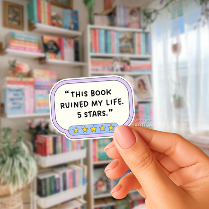 Hand holding a sticker with 'This book ruined my life. 5 stars'  text in a library setting