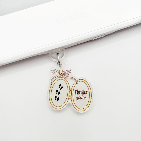 Locket design dust plug charm with 'thriller girlie' text, laying flat on a white background