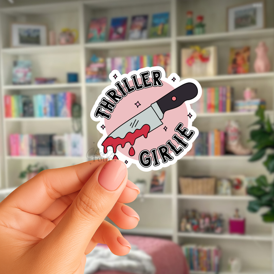 Hand holding a 'Thriller Girlie' sticker with a knife graphic against a blurred bookshelf background.
