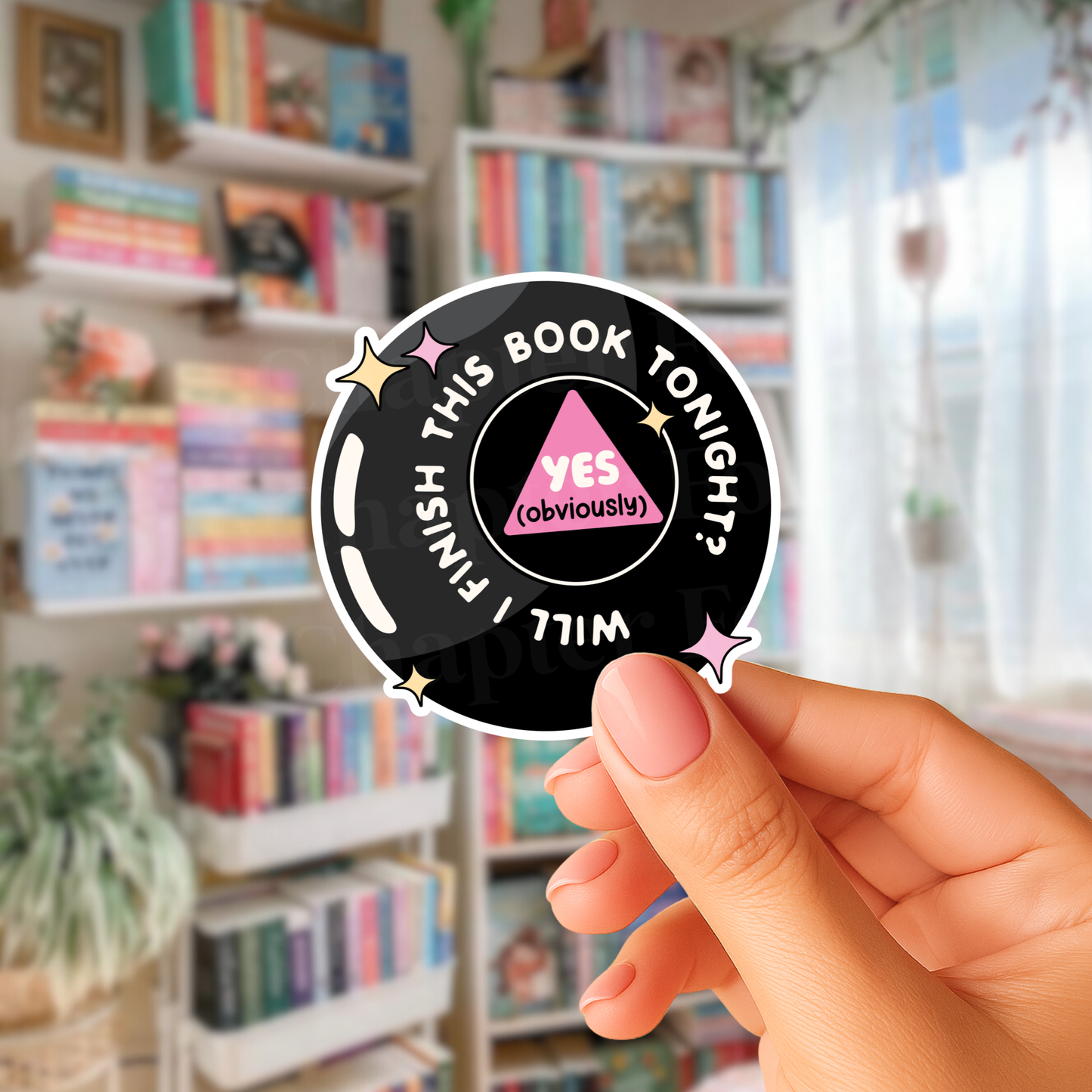 Hand holding a sticker with text 'Will I finish this book tonight? Yes, obviously' with a blurred bookcase in the background