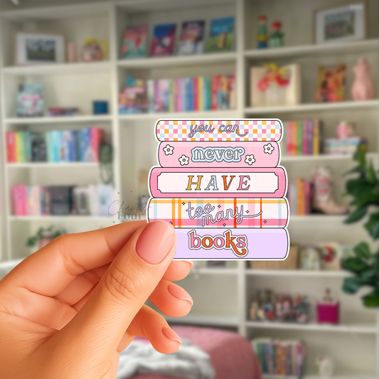 Stack of colorful books sticker with 'You can never have too many books' text, held by a hand in front of a bookshelf.