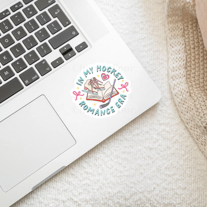 Laptop with a 'In My Hockey Romance Era' sticker on a textured surface