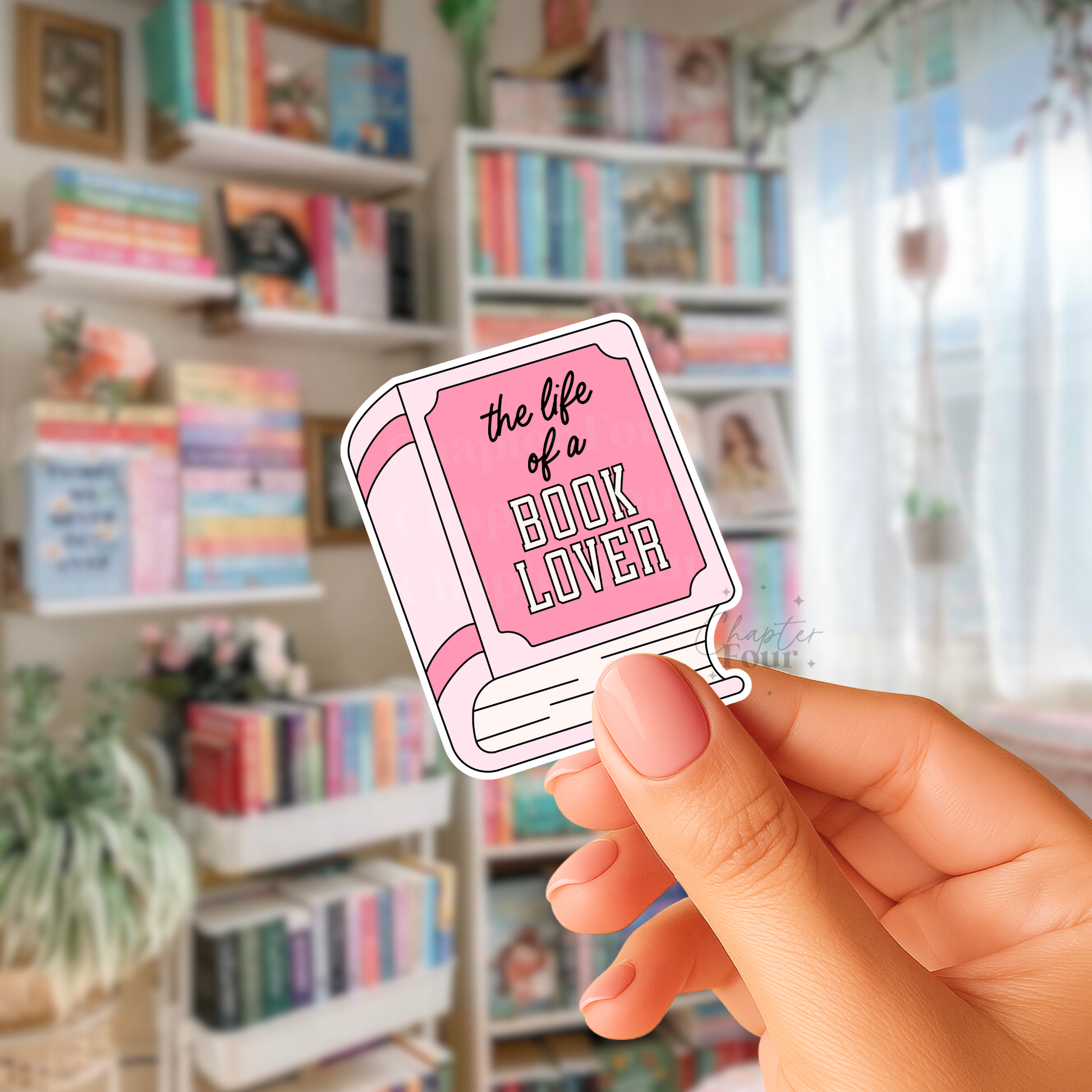 Hand holding a pink  book-shaped sticker with 'the life of a book lover' text in a bookstore setting