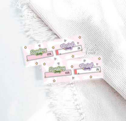 Two bookmarks with 'Reading Battery 100% Social Battery 2%' text, laying on a white blanket