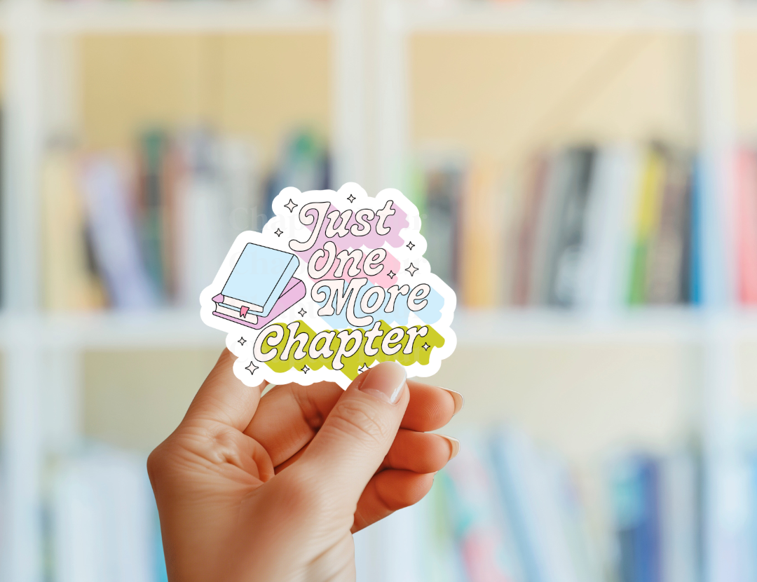 Hand holding a sticker with 'Just One More Chapter' text in front of a blurred bookshelf background