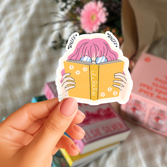 Sticker of a person with pink hair reading a book held by a hand, with books and flowers in the background.
