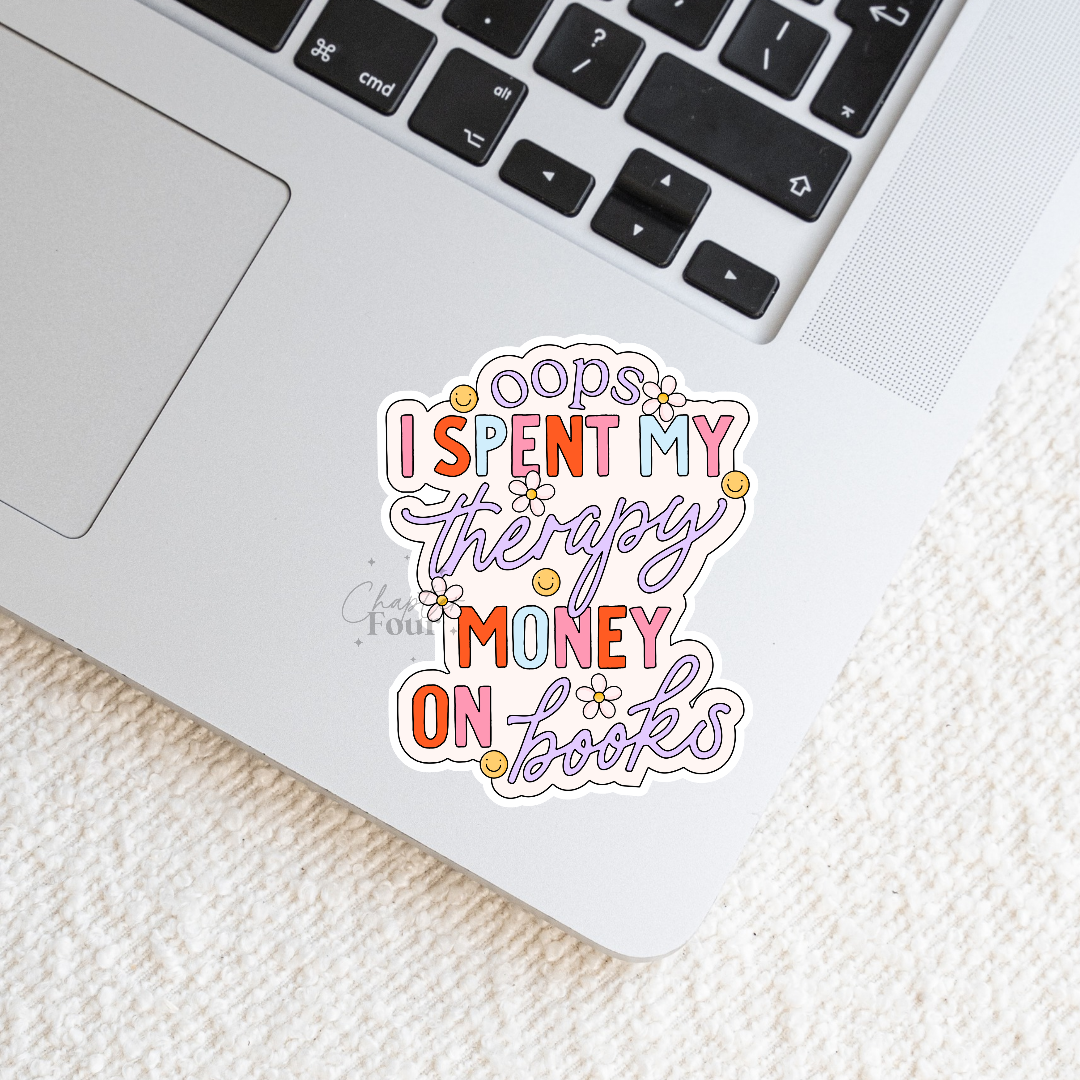 Colorful sticker with text 'oops I spent my therapy money on books' laying flat on a laptop.