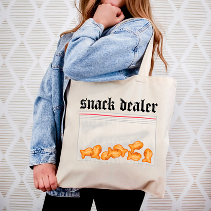Person holding a tote bag with 'Snack Dealer' text and snack graphics against a textured white background